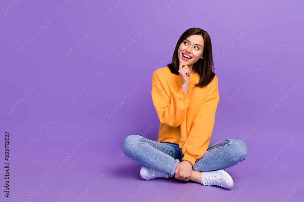 Full length photo of pretty lady sit leg crossed arm touch face interested look empty space sale ad isolated on purple color background Full length photo of pretty lady sit leg crossed arm touch face interested look empty space sale ad isolated on purple color background