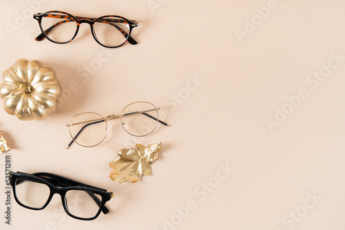 Eyewear fashion autumn collection. Trendy glasses in plastic and matallic frame on a beige background with golden leaves. Fall fashionable accessories. Optic store discount, sale. Copy space