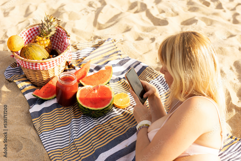 Cheerful young woman enjoy at tropical sand beach. Young woman taking a picture of fruit on the beach.. Cheerful young woman enjoy at tropical sand beach. Young woman taking a picture of fruit on the beach..