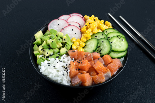 Salmon poke bowl: avocado, cucumber, corn, radish. Buddha bowl: rice, salmon, vegetables on a gray background.  photo