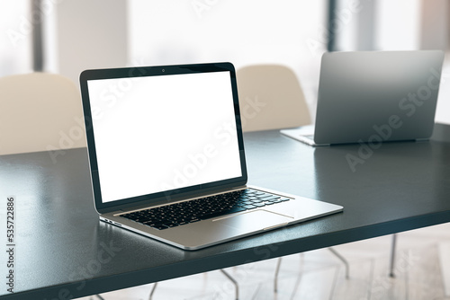 Close up of empty white laptop on dark desktop, mock up place on screen, blurry office interior background. 3D Rendering.