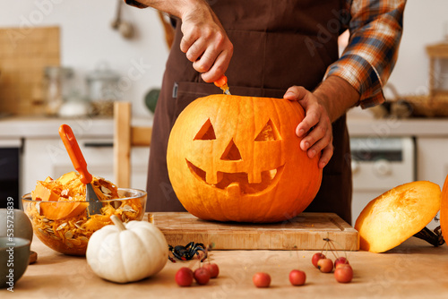 Photography Man in apron standing in kitchen and carving large orange Halloween pumpkin