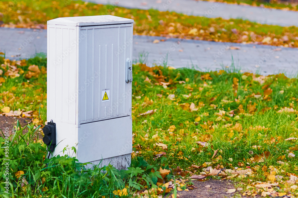 Electrical panel on a grassy lawn in autumn. Freestanding power distribution device. Yellow and orange leaves on green grass. Copy space. Selective focus Electrical panel on a grassy lawn in autumn. Freestanding power distribution device. Yellow and orange leaves on green grass. Copy space. Selective focus