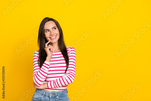 Photo of nice young woman bite finger look minded empty ad banner space wear stylish striped clothes isolated on yellow color background