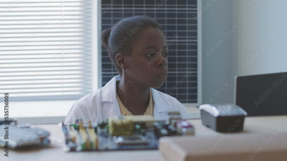 Serious African American female electronics engineer working with motherboards and solar panels in laboratory Serious African American female electronics engineer working with motherboards and solar panels in laboratory