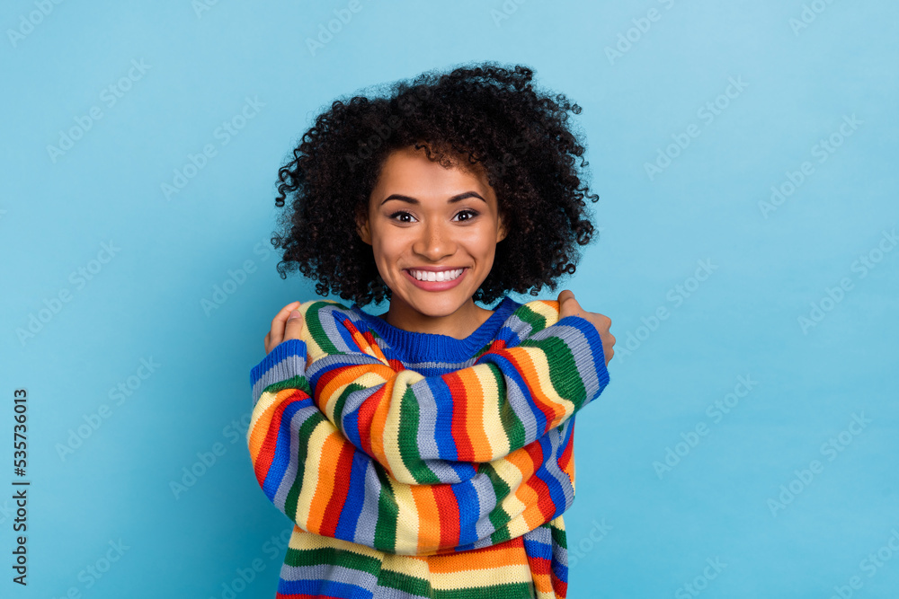 Photo of young curly hairdo lady hug herself wear colorful sweater isolated on blue color background Photo of young curly hairdo lady hug herself wear colorful sweater isolated on blue color background