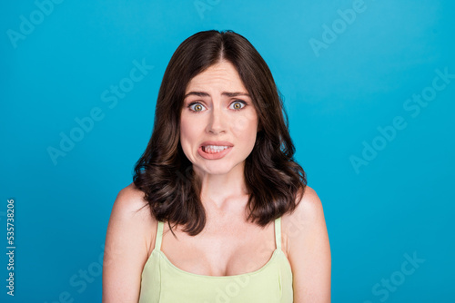 Photo of afraid guilty girl dressed green clothes biting lip empty space isolated blue color background