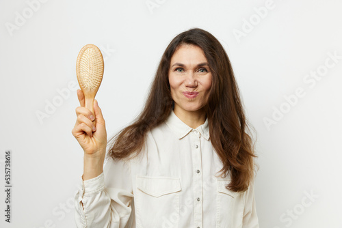 a sweet, pleasant, beautiful woman with well-groomed hair, standing on a light background holding a comb in her hands. Horizontal photo with an empty space for text