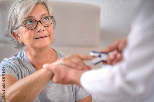 Senior Caucasian woman sitting in the medical center while the doctor measures the amount of oxygen in her blood using the oximeter