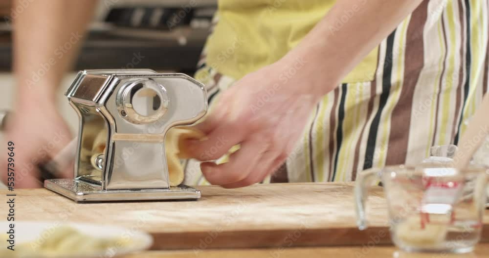 Male home cook making pasta sheets on a pasta machine in his kitchen. Closeup shot. Male home cook making pasta sheets on a pasta machine in his kitchen. Closeup shot.