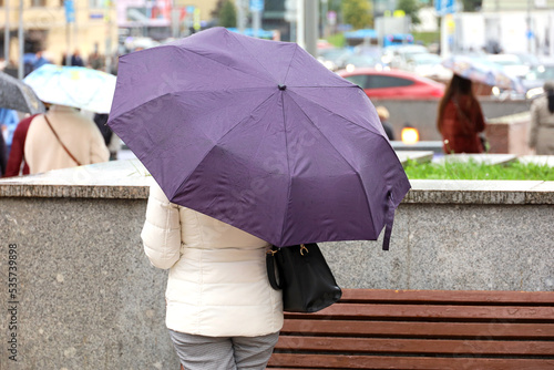 Rain in city, slim woman with umbrella standing on а street on people and cars background. Rainy weather in autumn