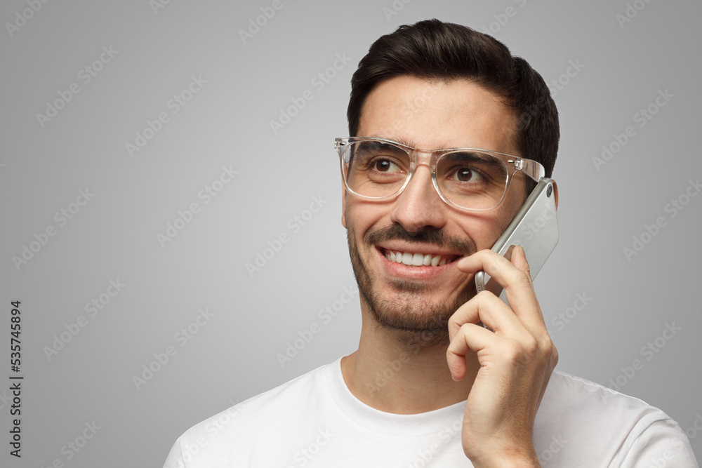 Man in trendy transparent glasses and white T-shirt having conversation on phone, smiling friendly Man in trendy transparent glasses and white T-shirt having conversation on phone, smiling friendly