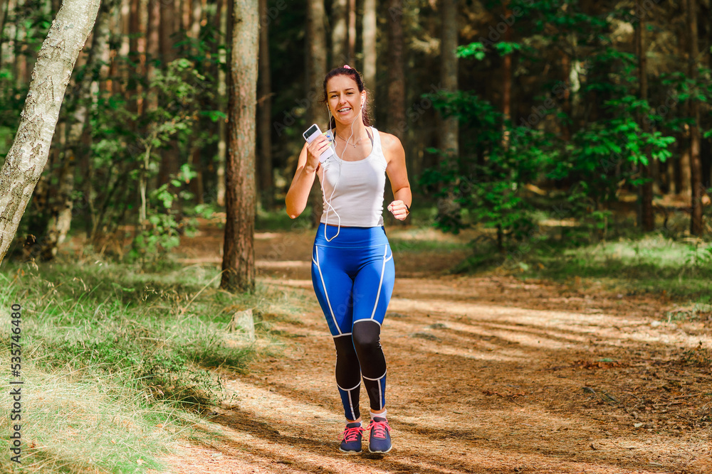 Young pretty woman running in the park at summer morning.The girl is listening to music while running.Sport and health nature concept Young pretty woman running in the park at summer morning.The girl is listening to music while running.Sport and health nature concept