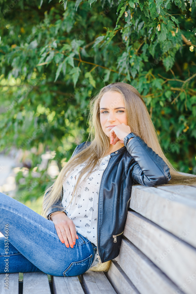 Obraz premium A beautiful fashion young city woman sitting on a bench.Summer,autumn day.Klaipeda,Lithuania.09-02-2022.
