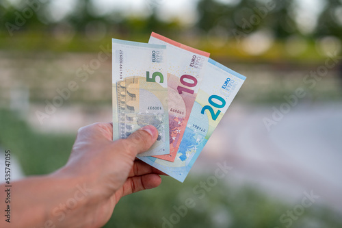 First person top view photo of hands holding fan of Euro banknotes on park background