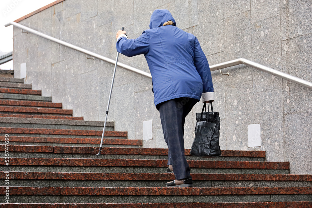 Old woman with walking cane climbing stairs outdoor. Concept for disability, limping adult, diseases of the spine Old woman with walking cane climbing stairs outdoor. Concept for disability, limping adult, diseases of the spine