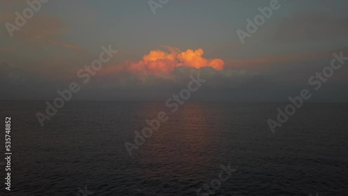 Golden sunrise reflects off single cloud over flat calm ocean horizon photo