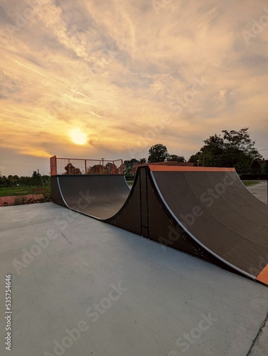 Vertical shot of half pipe in a skate park on bright sunset sky background