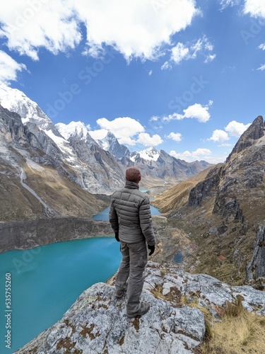 Vertical shot of a male standng on the rocks of Cordillera Huayhuash hiking circuit, Peru photo