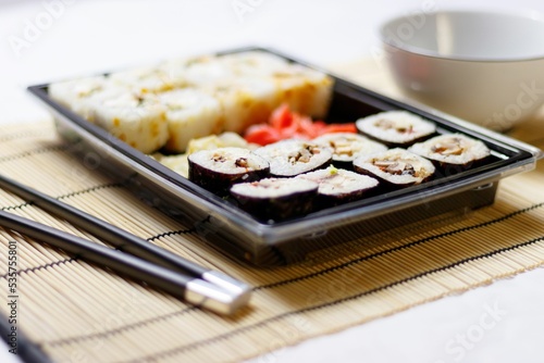 Set of red ginger rolls with a soy sauce bowl and black chopsticks on a bamboo mat