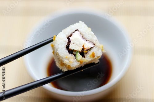 Japanese food roll picked up with black chopsticks with a soy sauce bowl in the background