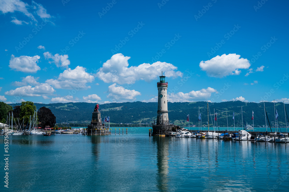 Germany, Lindau island city harbor lighthouse and boats anchoring in beautiful mountain panorama in water of bodensee lake on sunny day