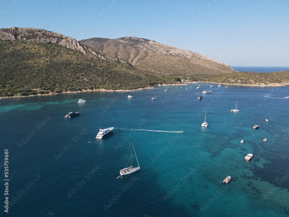 Obraz premium Aerial view of Cala Moresca and Figarolo Island in Golfo Aranci, north Sardinia. Birds eye from above of yacht, boats, crystalline and turquoise water. Tavolara Island in the background, Sardegna.