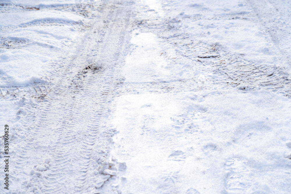 Texture of white winter country road, tire tracks and shoe prints in snow