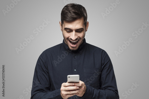 Young business man looking at phone with surprise, isolated on gray background