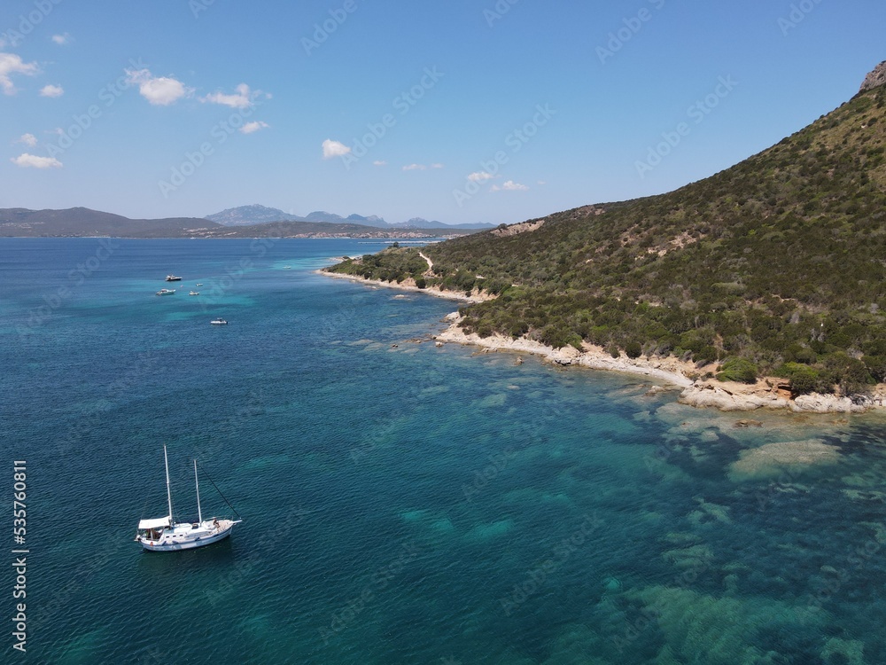 Aerial view of Cala Moresca and Figarolo Island in Golfo Aranci, north Sardinia. Birds eye from above of yacht, boats, crystalline and turquoise water. Tavolara Island in the background, Sardegna.