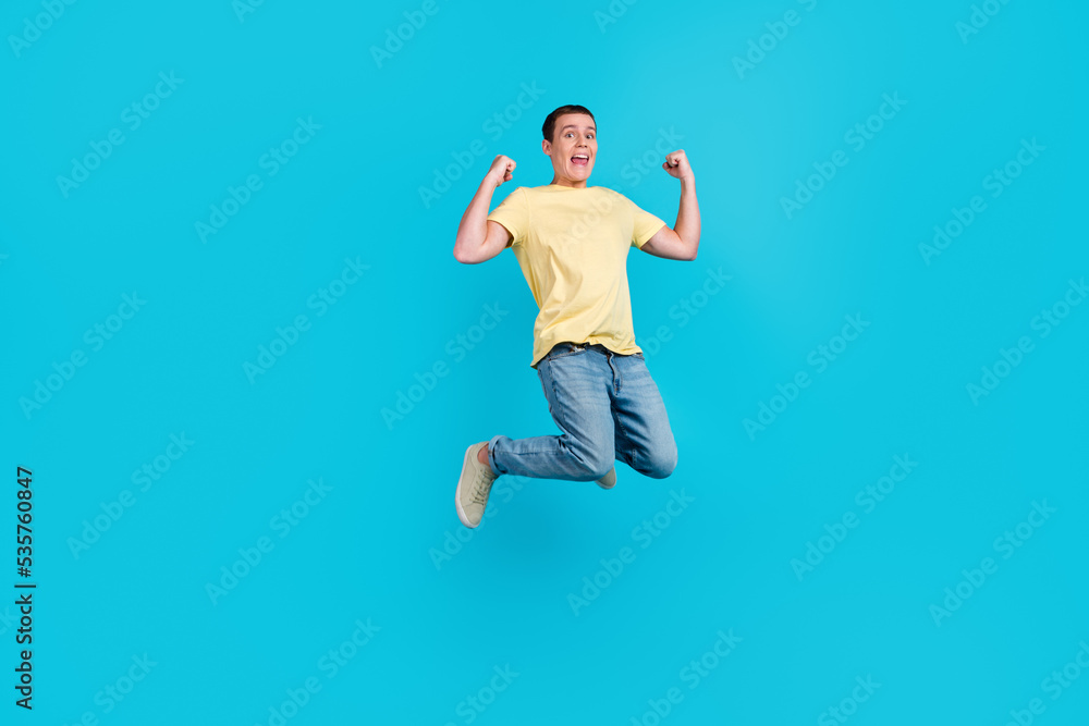 Full length photo of excited young man in t-shirt jumping while celebrating success isolated over blue color background