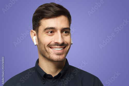 Portrait of smiling business man listening to music or radio, uses modern wireless earphones