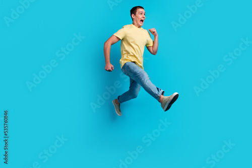 Full length photo of excited young man in t-shirt jumping running hurry discounts isolated over blue background