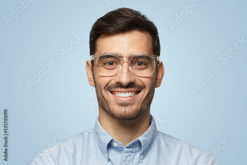 Smart businessman smiling at camera, in transparent glasses, isolated on blue background