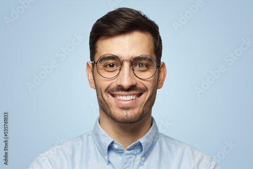 Portrait of businessman smiling at camera in round glasses, isolated on blue background