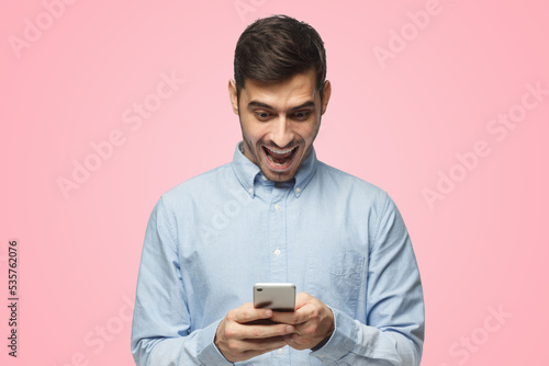 Young businessman looking at phone with surprise expression, isolated on pink background