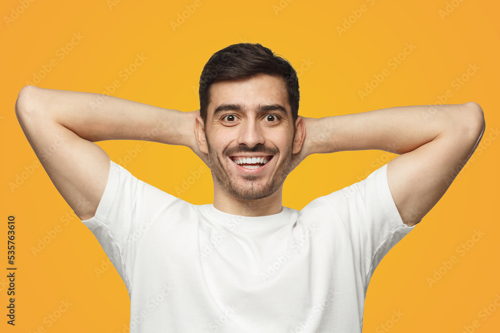 Young man standing isolated on yellow background with arms behind head, relaxing Young man standing isolated on yellow background with arms behind head, relaxing