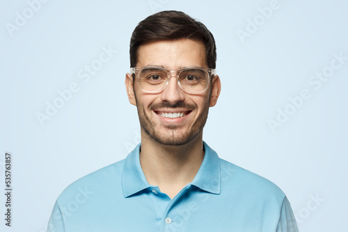 Smiling modern nice guy in polo shirt and trendy trasparent glasses, isolated on blue background © Damir Khabirov