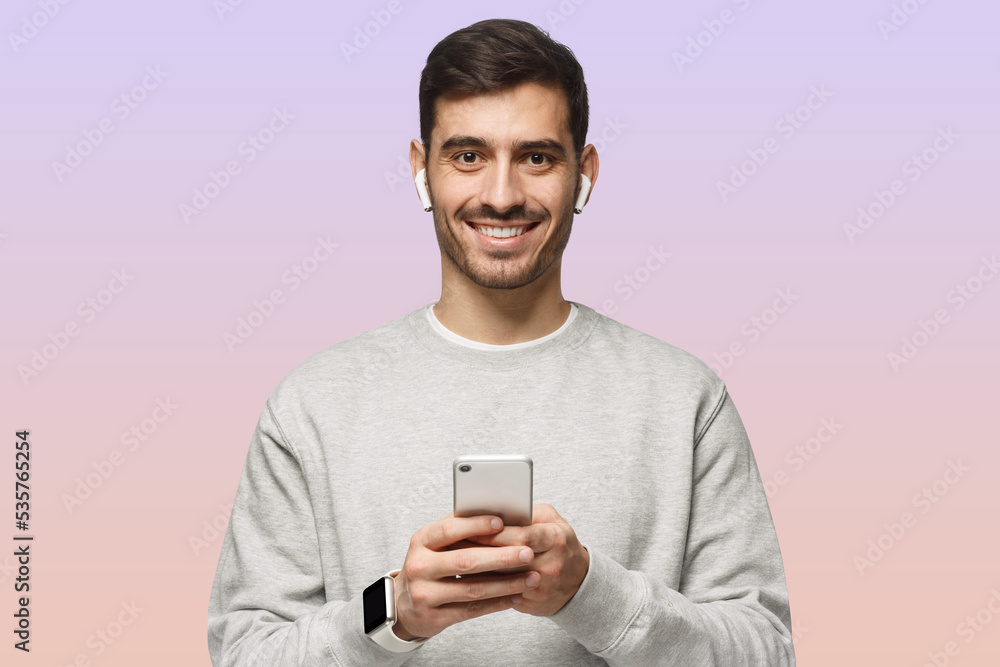 Young man looking at camera with smile, holding smartphone with both hands Young man looking at camera with smile, holding smartphone with both hands