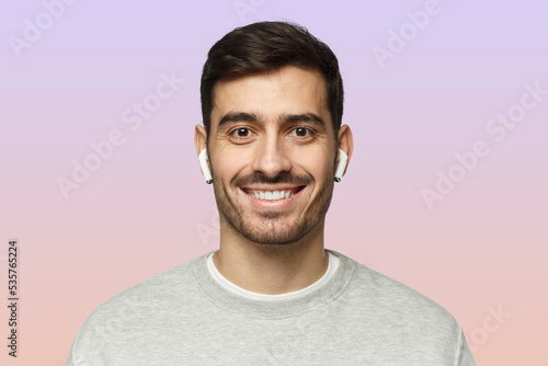 Close-up portrait of young smiling handsome man with earphones isolated on pink © Damir Khabirov