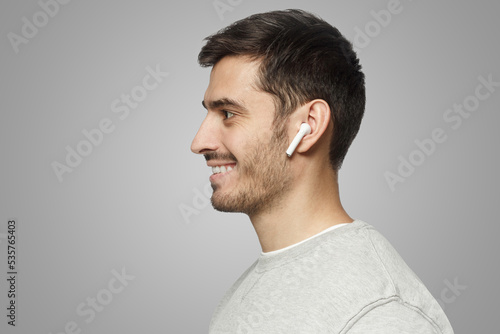 Sideways portrait of smiling man listening to music or radio in modern wireless earphones