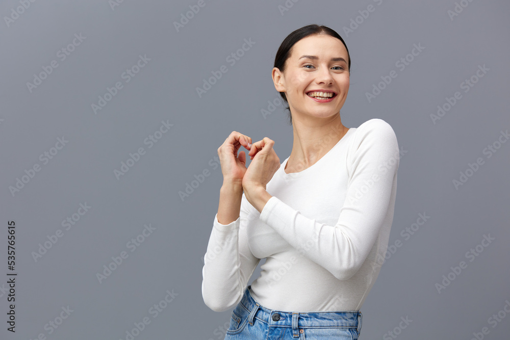 an attractive woman stands on a gray background in a white T-shirt, happily made a heart out of her hands an attractive woman stands on a gray background in a white T-shirt, happily made a heart out of her hands