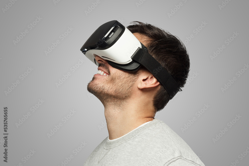 Young man wearing virtual reality headset, looking up on gray background Young man wearing virtual reality headset, looking up on gray background