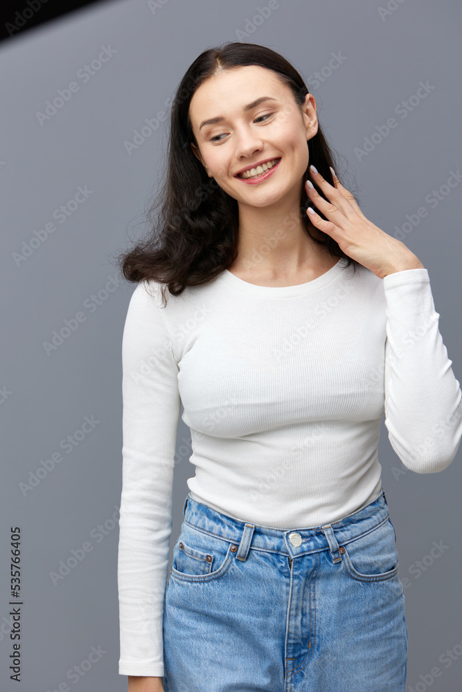 a gentle woman stands on a dark background in a tight white T-shirt, stealthily looks down holding her hair with her hand a gentle woman stands on a dark background in a tight white T-shirt, stealthily looks down holding her hair with her hand