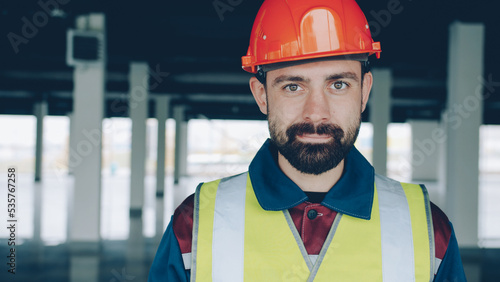 Bild auf Leinwand portrait of builder in uniform looking at camera and nodding head smiling standing indoors in plant