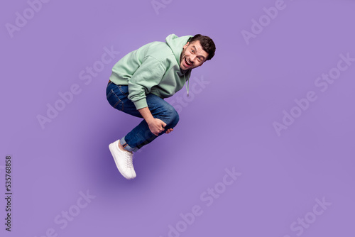 Full length profile photo of overjoyed cheerful person hands hold knees flying fall down isolated on violet color background