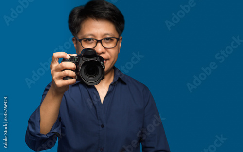 Portrait of a woman with short black hair holding a digital camera while standing on a blue background