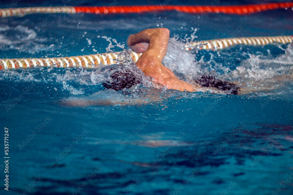 A swimmer at a competition quickly swims in a pool in clear blue water among the tracks	
