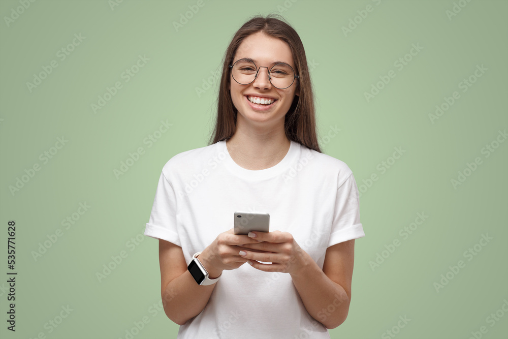 Beautiful girl in transparent glasses exchanging mesages on phone, isolated on green Beautiful girl in transparent glasses exchanging mesages on phone, isolated on green