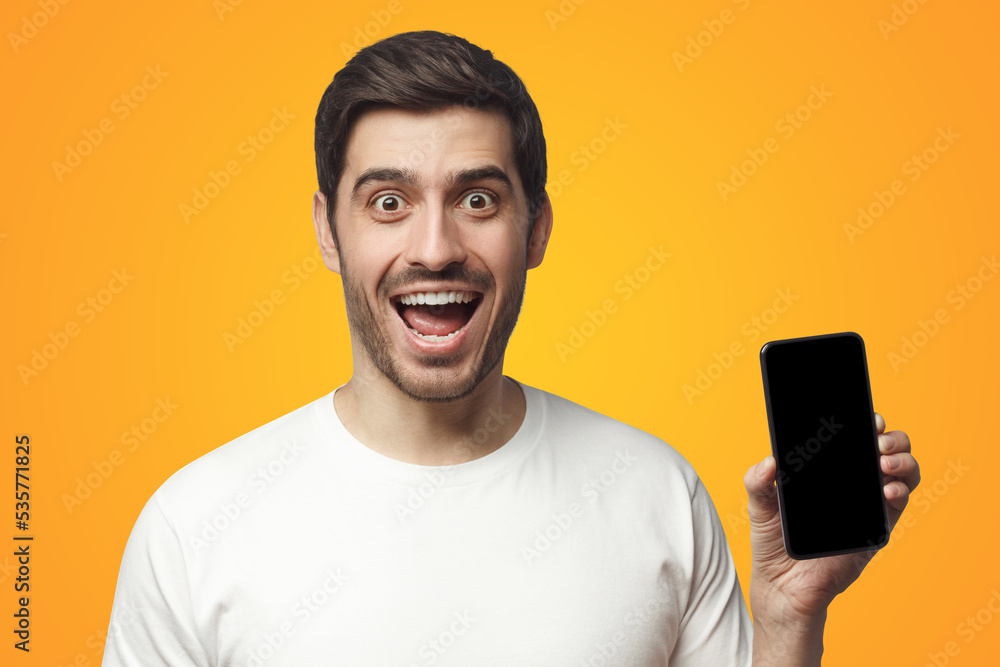 Excited young man holding blank phone with empty black screen, screaming WOW Excited young man holding blank phone with empty black screen, screaming WOW